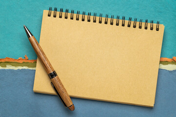 blank spiral sketchbook with a pen against colorful abstract landscape