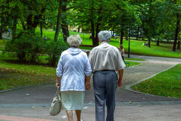 Elderly couple holding hands and walking in city autumn green park