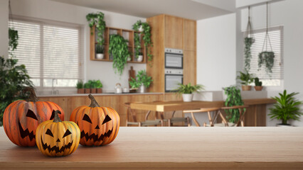 Obraz premium Halloween carved pumpkins on wooden table. Autumn decoration over interior design scene. Wooden modern kitchen with houseplants, urban jungle interior design concept