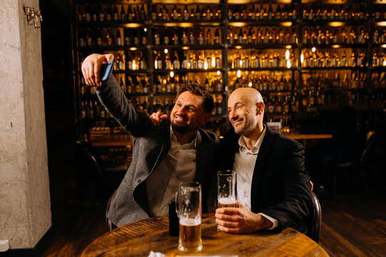 friends drinking beer and taking selfie with smartphone in bar or pub. male friendship - happy.