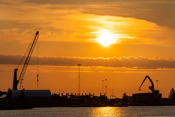 Port cranes at sunset. Cargo transportation and cargo ships.