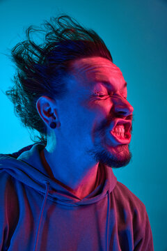 Funny portita of man posing with wind blowing into face against blue studio background in neon light. Concept of human emotions, facial expression, lifestyle. Meme look