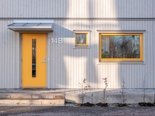 Modern yellow apartment entrance door with side windows, stone stairs and metal rain cover