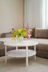 Interior design warm beige sofa and white round table with colourful flowers on the white carpet