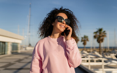 Fototapeta premium young pretty curly woman in sunglasses on summer vacation with phone