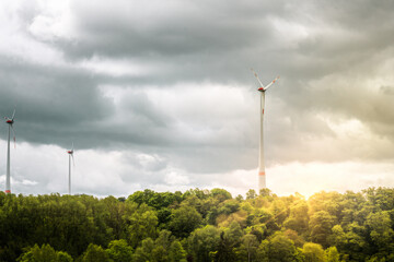 drehende Windräder produzieren Energie neben grünen Bäumen und einen düsteren blauen Himmel