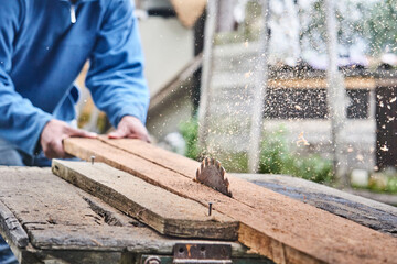 Crop anonymous carpenter sawing wooden board in farmland