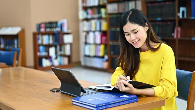 Happy female student using digital tablet, searching data information and taking notes. Education, learning and technology