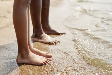 Close-up of barefoot dad standing on sand near the water together with his child