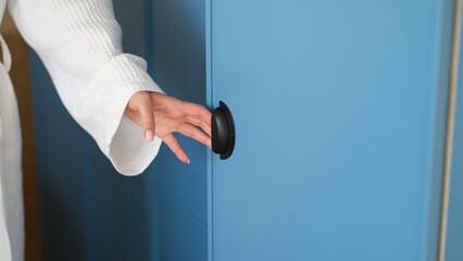 Woman in white bathrobe opening door of blue wardrobe in hotel with hand closeup. Custom furniture concept