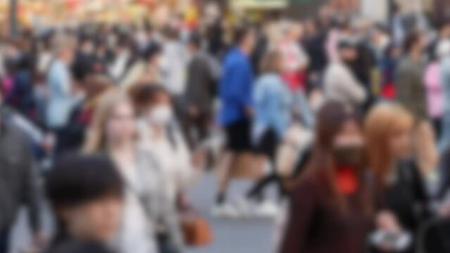 Blurred defocused view of the Shibuya Crossing in Japan becomes a hive of activity as countless people traverse the intersection during daylight hours.
