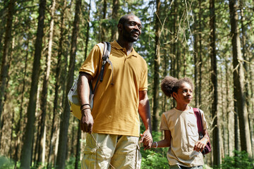 African American dad walking in the forest with his little child during their camping