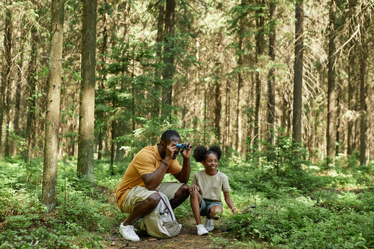 Dad looking through binoculars while hiking with his daughter in the forest - Powered by Adobe