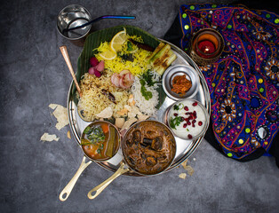 South Indian vegetarian thali consisting of  a variety of rice dishes, eggplant and mushroom curry, rasam, pickles, raita, Traditional Indian table setting.