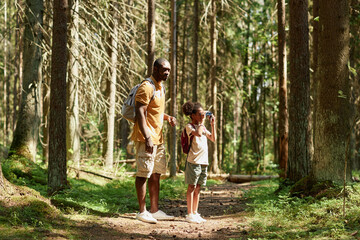 Little girl looking through binoculars during travelling with her dad in the forest