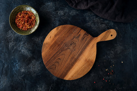 Top view of a beautiful cutting board, a bowl of red spices, and a decorative cloth on a dark blue background.
