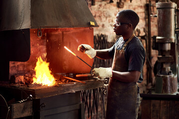 Blacksmith, fire and a black man melting metal in a workshop for manufacturing or industrial design. Factory, welding or industry with a male designer in metalwork using a hot flame to melt material