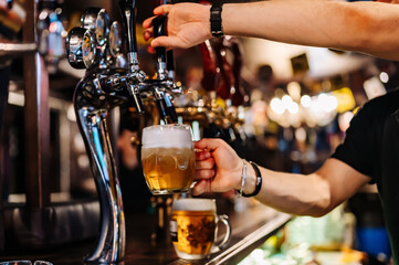Fototapeta na wymiar man bartender hand at beer tap pouring beer in glass in bar or pub