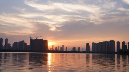 The beautiful sunset view with the buildings' silhouette and orange color sky mirrored in the...