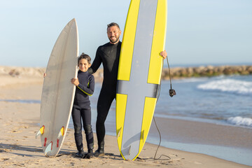 A family of surfers - smiling father and son standing on the seashore with their surfing boards
