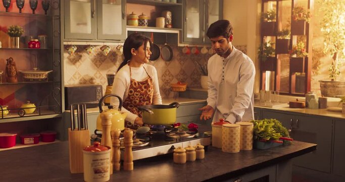 Beautiful Indian Couple Preparing Food in Kitchen: Girl Experimenting with Flavors, Discovering New Recipes, Cooking with Passion. Funny Young Man Fooling Around Juggling Vegetables. Wide Zoom In