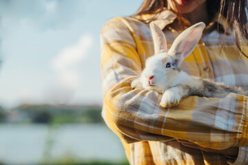 Closed up rabbit over woman arm with pond and forest blur background, human and pet love and warm...