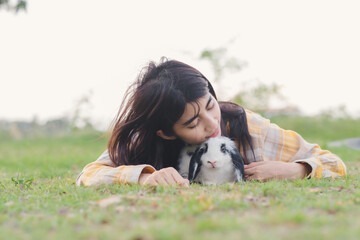 Portrait of black and white rabbit in backyard with woman lay down on green grass floor playing together. - Powered by Adobe