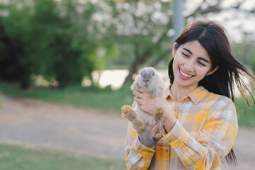 Asian woman in scotish shirt holding grey rabbit walking outside with smile of happiness at plublic park.