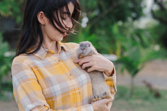 Asian woman embrass gray cute rabbit that scaring of something with love and dedicated while walking in garden, relationship between human and pet