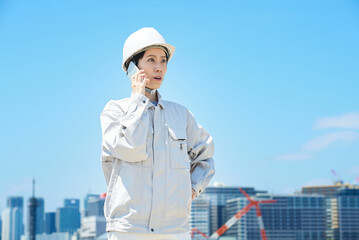スマートフォンで通話する作業服姿の女性