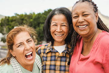 Happy multiracial elderly friends smiling in front of camera - Senior women hugging each other outdoor