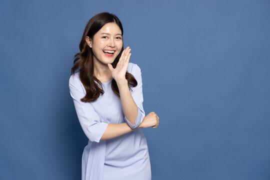 Asian businesswoman with open mouths raising hands screaming announcement isolated on blue background