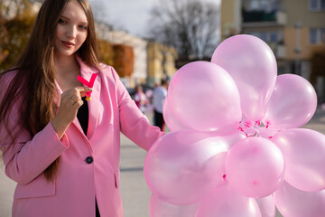 A girl with pink balloons holds a pink ribbon and promotes preventive breast examinations.