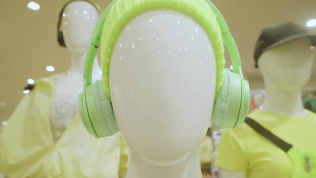 Close-up of mannequin wearing a lime green color hat and headphones and urban style clothes stand in the clothing store. 4K