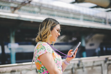 Happy traveler using a smartphone in a train station while is waiting for transport
