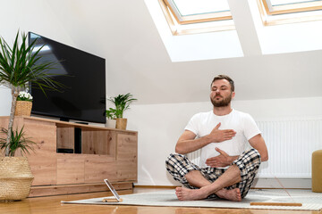 Man doing breathing exercise sitting on floor at home in half lotus position.	
