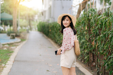 Obraz premium Portrait of asian young woman traveler with weaving hat and basket happy smile on green public park nature background. Journey trip lifestyle, world travel explorer or Asia summer tourism concept.
