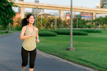 Fototapeta premium Fit Asian young woman jogging in park smiling happy running and enjoying a healthy outdoor lifestyle. Female jogger. Fitness runner girl in public park. healthy lifestyle and wellness being concept