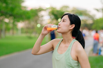 Female jogger. Fit young Asian woman with green sportswear drinking organic orange juice after running and enjoying a healthy outdoor. Fitness runner girl in public park. Wellness being concept