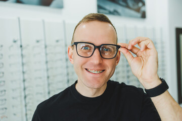 A young smiling man chooses glasses for vision correction in an ophthalmology salon. Glasses for vision correction.