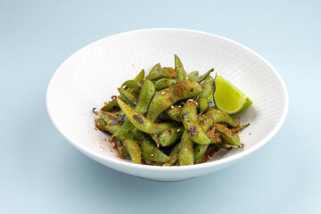 Portion of green edamame beans salad with lime on blue background