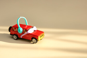 red toy car in sunglasses and headphones drives towards the sunlight on a light beige background with copy space