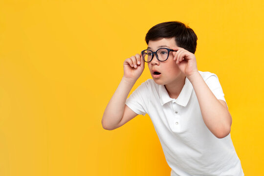 little asian boy with glasses looks away in surprise on yellow background, korean child looks in amazement at copy space