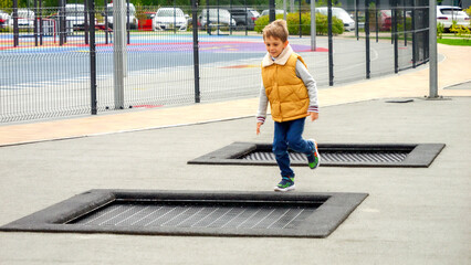 Little boy running on public playground and jumping over trampolines. Active child, sports and development, kids playing outdoors.