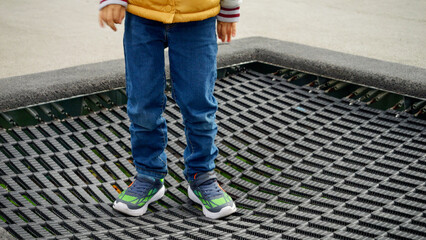 Closeup of child wearing sneakers jumping high on the trampoline. Active child, sports and development, kids playing outdoors