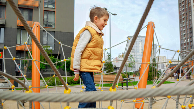 Cheerful smiling boy playing and rocking on the swing with ropes and nets. Active child, sports and development, kids playing outdoors