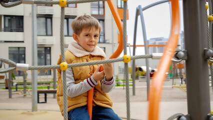 Happy smiling boy enjoys spinning on carousel at new public playground. Active child, sports and development, kids playing outdoors