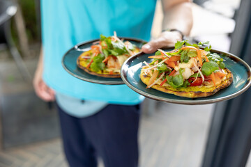 Waiter hold plate with fresh salad on a grilled flatbread