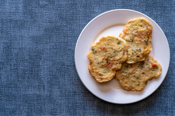Saltfish fritters on a white ceramic plate isolated on a textured blue background. A traditional Jamaican dish often referred to as stamp and go.