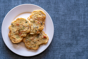Saltfish fritters on a white ceramic plate isolated on a textured blue background. A traditional...